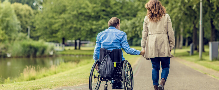 A man in a wheelchair holds hands with a woman walking