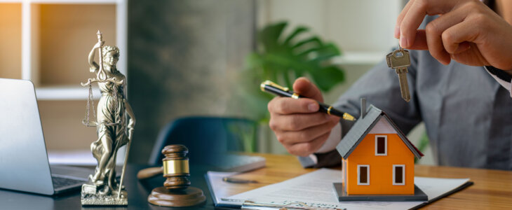Judge holding wooden judge hammer against house background and businessman documents and house model on wooden table Real estate disputes and property auction concept