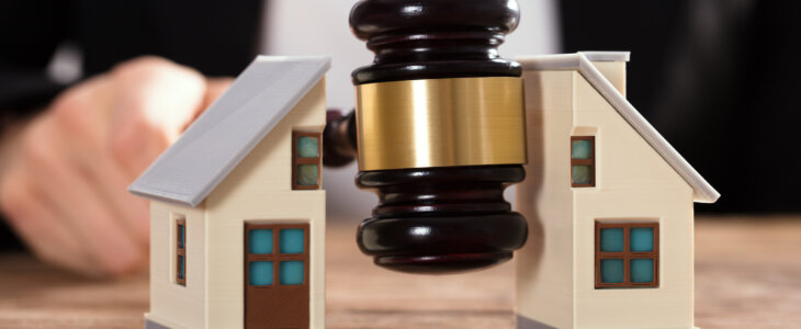 Close-up Of A Judge Striking Gavel Between Split House Over Wooden Desk